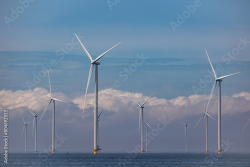 Wind farm of wind mills, generators, wind turbines, off shore in a sea or lake IJsselmeer in the Netherlands. Multiple tall windmills and rotor blades generating green sustainable energy, electricity