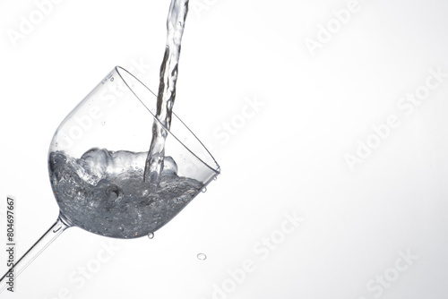 Splash in glass, transparent glass receiving water, white background, selective focus © Milton Buzon