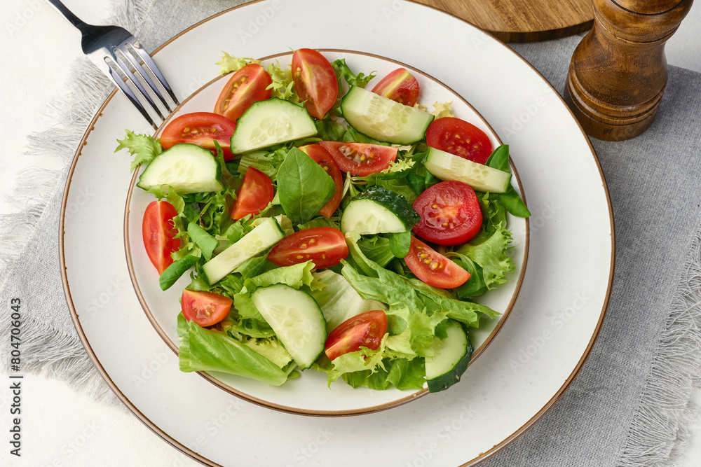 Salad of chopped cherry tomatoes and cucumbers in a white round plate on the table, healthy food