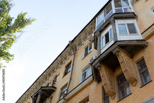 Low angle side view of ornate balcony on faded residential building against clear summer sky in Volgograd, Russia. Soft focus. Old soviet architecture theme.