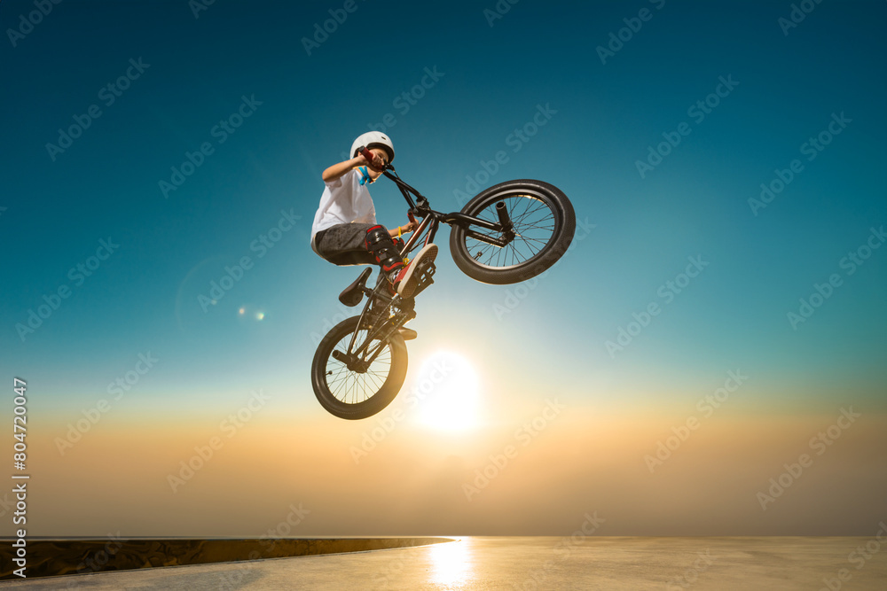 Fototapeta premium A teenager BMX Racing Rider performs tricks in a skate park on a pump track.