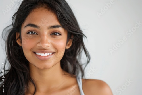Close up portrait of a beautiful, young attractive and elegant Indian Asian woman against a white background. She is in exercise attire and is smiling confidently. © Aliaksandr Siamko