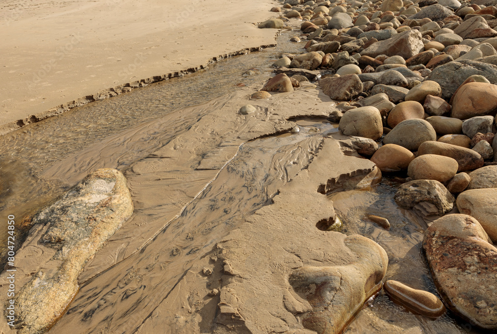 Obraz premium Water running inbetween large stone and rocks onto a beach