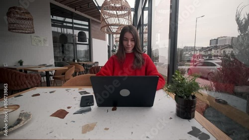 Portrait of a young girl who works as a freelancer on the veranda of a cafe. Computer work, Internet, remote work.