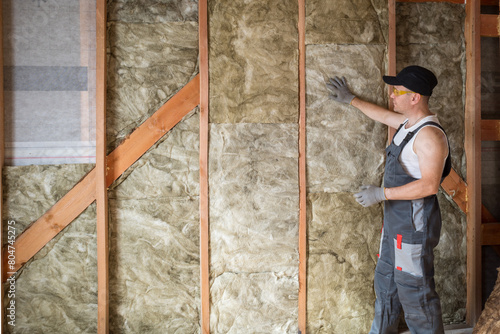 a construction worker insulates the wall of a frame house with mineral wool photo