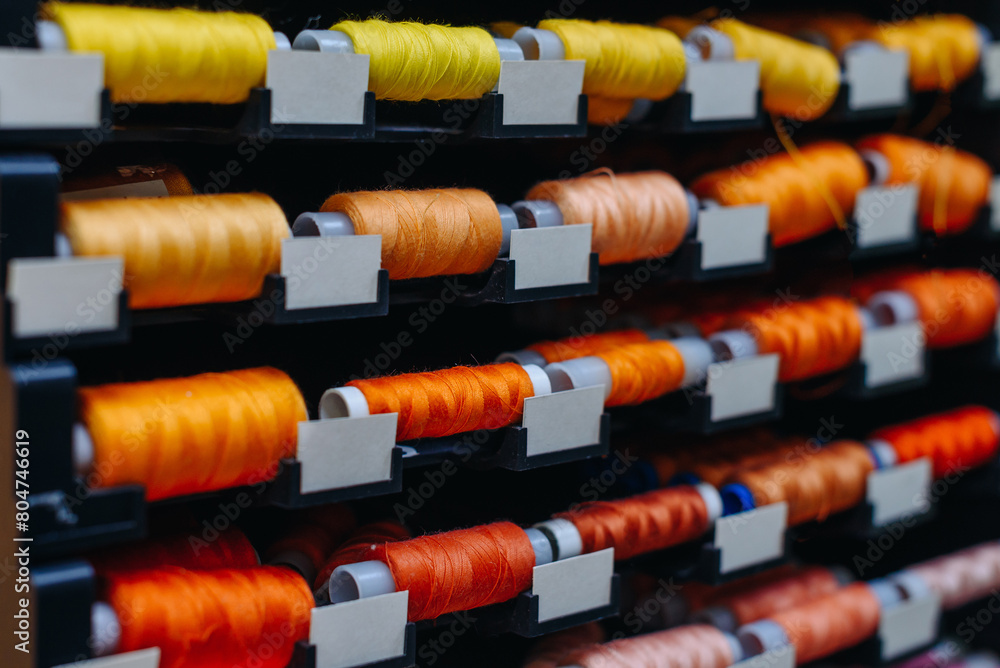 amount of different skeins of threads on special shelves in sewing studio or atelier, several colours, yellow and orange and red, handmade and sewing concept