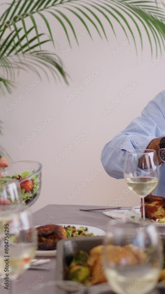 Vertical. Happy Caucasian family sitting at table passing food to each other at meal. People of diverse generations enjoying a family reunion together at weekend. Community and wellness at home Vertical. Happy Caucasian family sitting at table passing food to each other at meal. People of diverse generations enjoying a family reunion together at weekend. Community and wellness at home