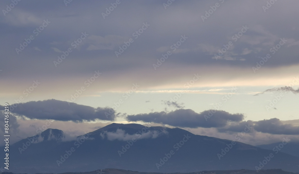 Obraz premium Nuvole bianche e grigie aggrappate come ovatta alle montagne in una giornata invernale al tramonto