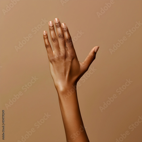 Single graceful hand with delicate fingers raised against a beige background