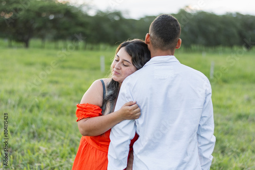 young latina woman hugging her boyfriend while leaning on his shoulder. man with his back turned.