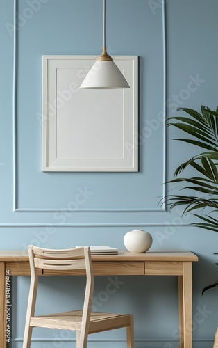A blank picture frame sitting on top of an empty desk, light blue wall with white trim, soft lighting from a lamp above the chair, light wood color, modern French country style interior design
