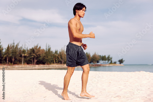 Smiling Asian Man Enjoying Beach Vacation: Torso of a Muscular Guy on Sandy Tropical Island, with Palm Trees, Blue Sky, and Crystal Clear Ocean Water.