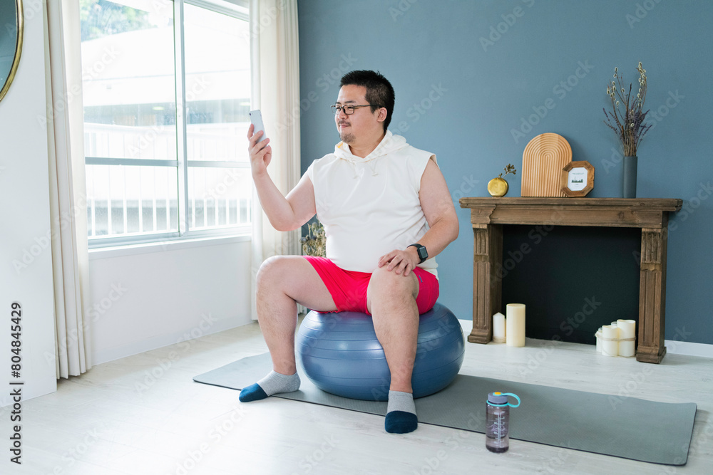 Obraz premium バランスボールに座りながらスマートフォンを見る大柄な日本人男性