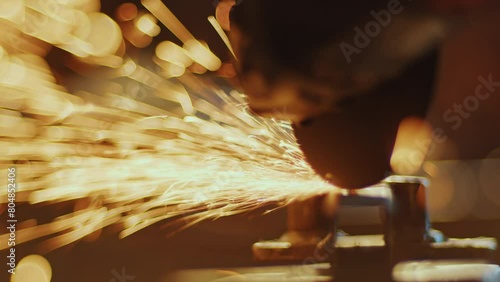 Close-up view of cutting metal billet with angle grinder disk producing fire sparks in blacksmith workshop photo