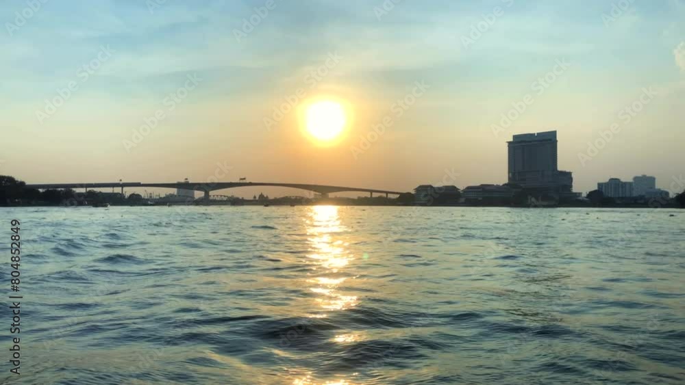 Sun setting over a river in a city. Sunset behind a large bridge on the Chao Phraya river. Bangkok, Thailand. Sun setting over a river in a city. Sunset behind a large bridge on the Chao Phraya river. Bangkok, Thailand.