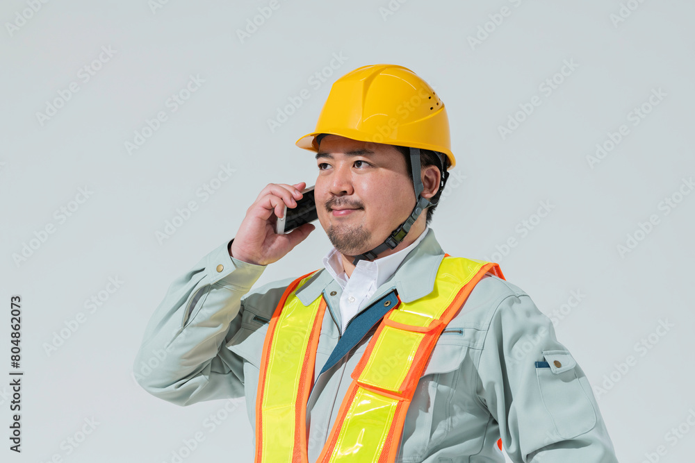 スマートフォンで電話をする作業服の男性