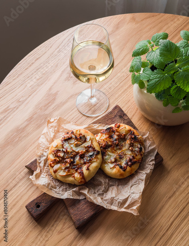 Delicious aperitif, appetizer, tapas - caramelized pear, gorgonzola, honey and walnuts mini pizza and a glass of white wine on a wooden table