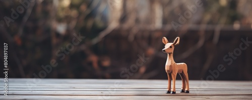 A wooden deer figurine stands on a wooden table. The background is blurry.