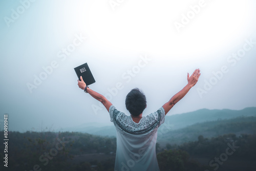Man raised both hands up and holding bible, pray for blessings to God. photo