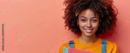 A beautiful young woman with curly hair smiles and holds many books on an isolated pastel peach background, in the style of a copy space concept for educational wordings, stock photo, teacher photo
