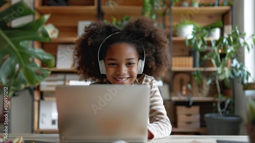 Happy schoolgirl doing homework at home. During pandemic or travel children continue learning process. Mixed-race KId receive assignments from teachers via laptop and headphones. photo