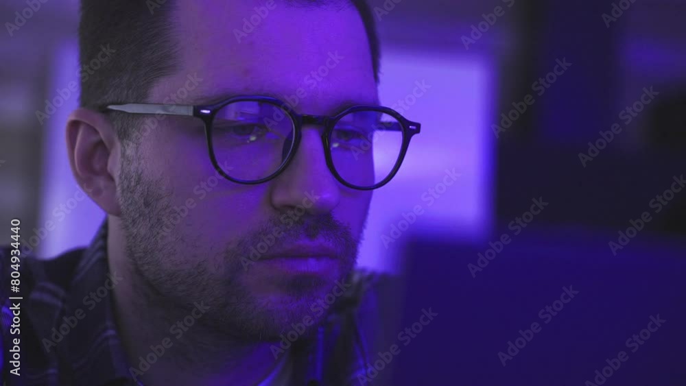 Young bearded man looking at screen in the dark room, watching dj party show Young bearded man looking at screen in the dark room, watching dj party show