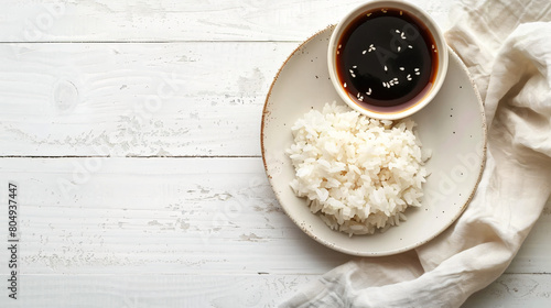 Plate with boiled rice and soy sauce on white wooden 