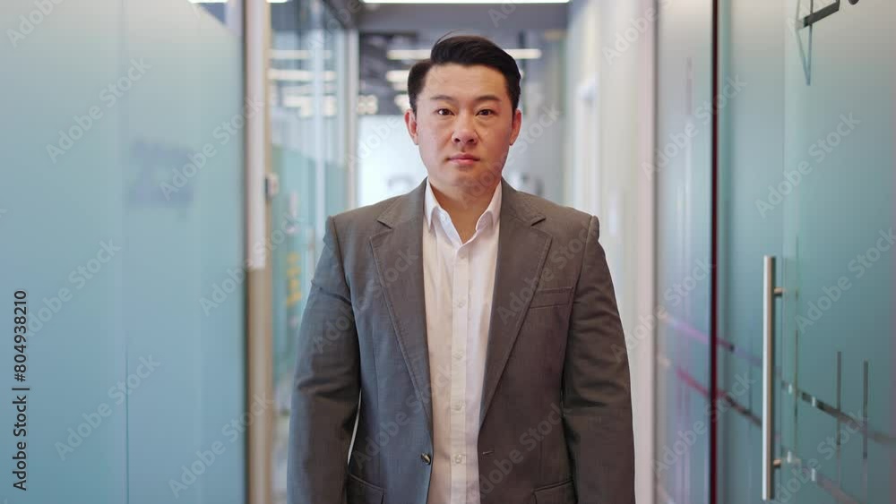 Successful man meeting camera with serious gaze while exuding determination in office corridor lined with glass-walled cabinets. Confident male dressed in office attire indoors. Concept of people. Successful man meeting camera with serious gaze while exuding determination in office corridor lined with glass-walled cabinets. Confident male dressed in office attire indoors. Concept of people.
