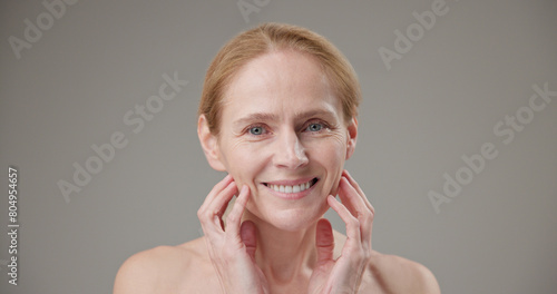 Real people age, beauty, health and dry skin care concept - beautiful mature Caucasian middle aged woman in her 50s touching facial skin doing facial massage and looking at camera © Anatoly Repin