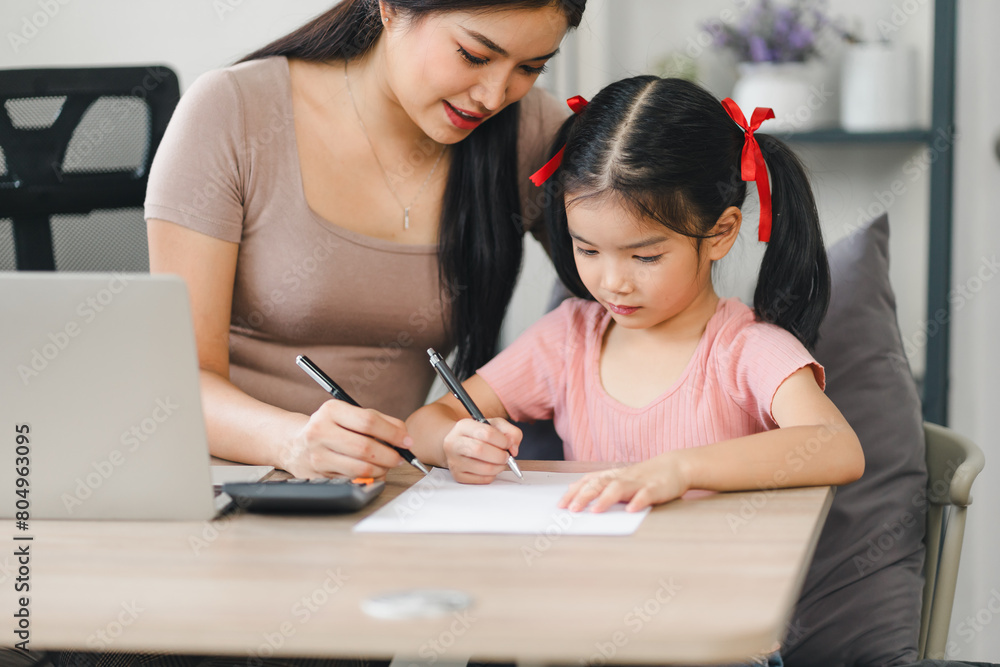 Mother helps daughter doing homework sitting at table writing in paper notebook right answer Mother helps daughter doing homework sitting at table writing in paper notebook right answer