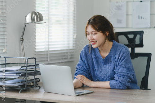 Focused young Asian businesswoman sitting and remote working on laptop computer in a modern home office. Distant workday concept.