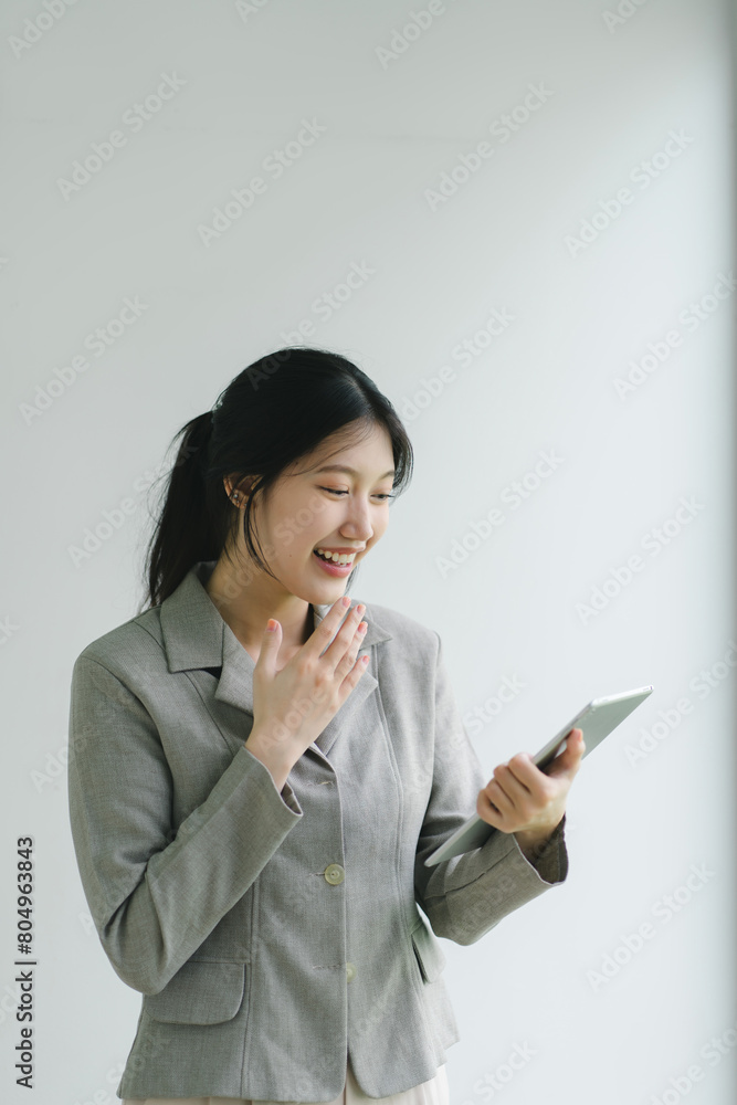 Confident Asian businesswoman smiling and using a digital tablet against a plain background. Confident Asian businesswoman smiling and using a digital tablet against a plain background.