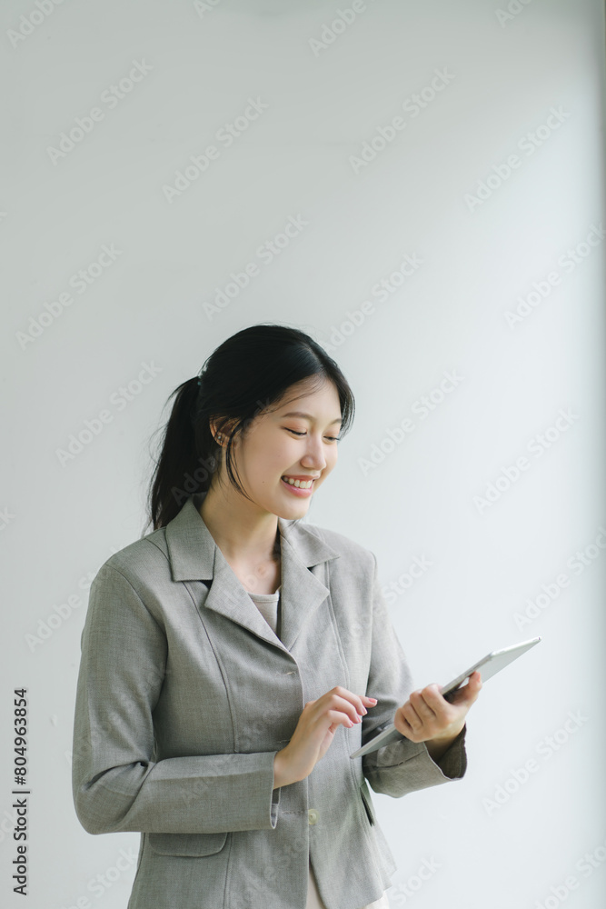 Confident Asian businesswoman smiling and using a digital tablet against a plain background. Confident Asian businesswoman smiling and using a digital tablet against a plain background.