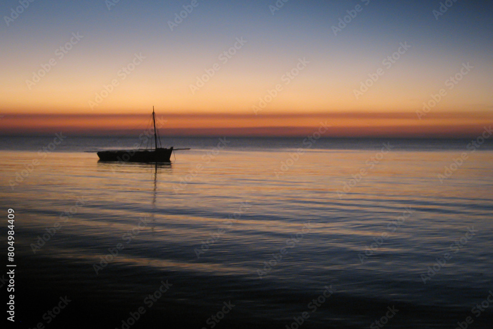 The silhouette of a dhow in the calm water of Maputo Bay in the early evening, as seen from Inhaca Island