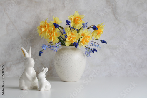 porcelain rabbits on the table and a bouquet of spring garden flowers in a vase. copy space. Easter still life.