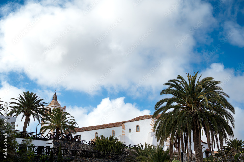 A cloudy sky with a white building in the background. The sky is mostly blue with a few clouds scattered throughout