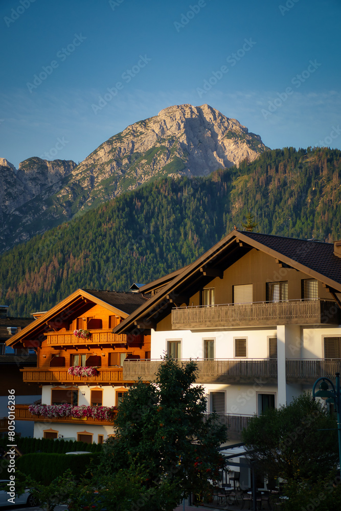 Zwei Häuser im goldenen Morgenlicht, mit Bergpanorama mit Wäldern und Gipfeln im Hintergrund