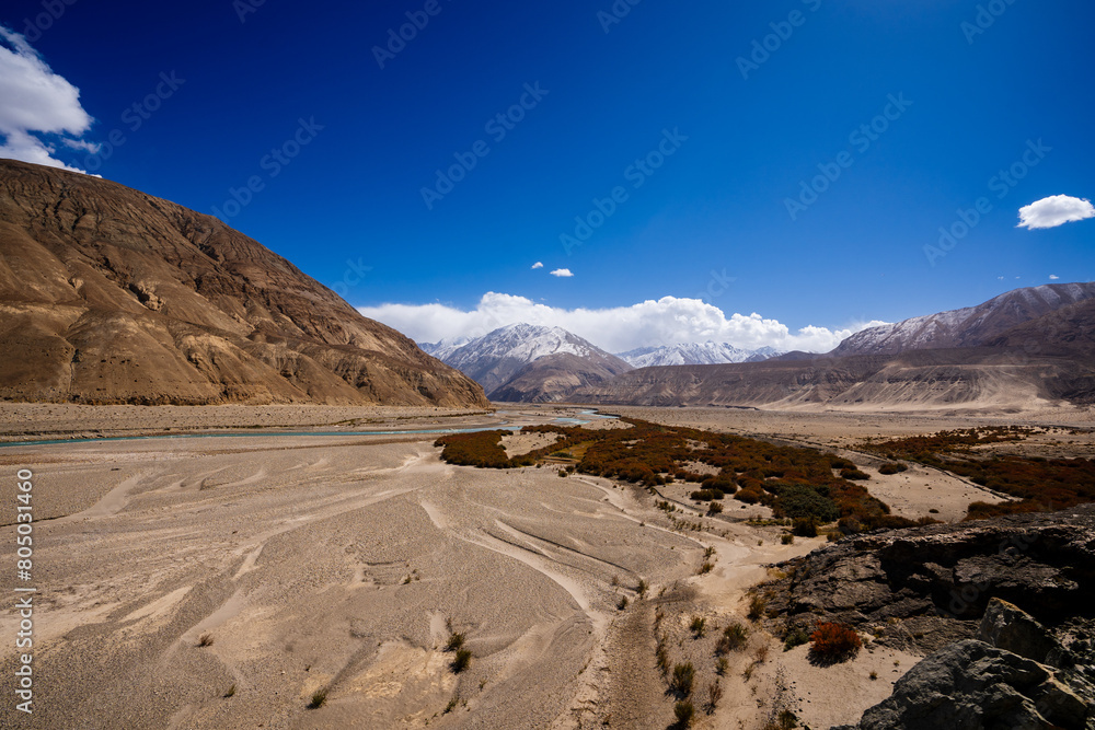 Fototapeta premium Vibrant view of the Indus River flowing through a barren Himalayan valley under a clear blue sky in Ladakh, India.