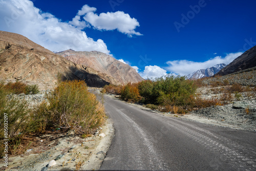 Spectacular high roads wind through rugged mountains beneath blue skies and the remote snow-capped peaks of Ladakh, India.