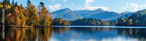 Serene landscape of a majestic mountain range by a tranquil blue lake with forested shores bathed in sunlight photo