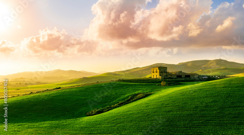 sceniv view at a nice farm in green fields in hills and highlands, landscape of spring green hills with mountain bright sunset on backdrop