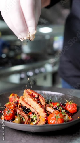 A professional chef decorating an octopus dish with sesame in a kitchen of a luxury restaurant in slow motion. Close-up, vertical footage.
