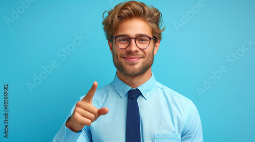 Young handsome business man in blue shirt with thumbs up finger on blurred office background. Business concept, happy top manager evaluates work his team