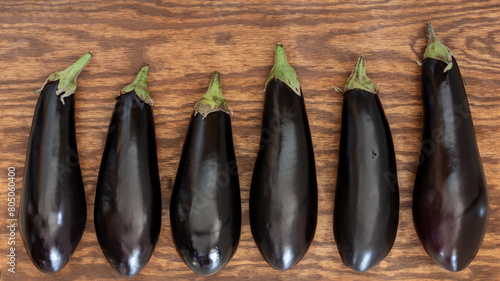 Six fresh, unpeeled eggplants on a brown wooden surface. Eggplants are a good meat substitute for vegatarians and vegans.