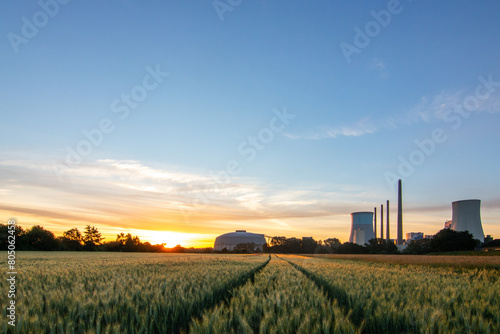 The morning in a wheat field in the background a coal-fired power station at sunrise. Landscape shot of nature and industry at the Staudinger power plant, Hainburg, Bavaria, Germany photo