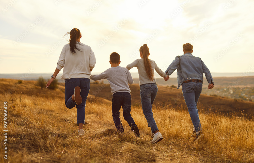 Fototapeta premium Big cheerful family playing at yellow field in nature at sunset. Sunset evening sky beautiful nature yellow field parents and children likes beauty of the outdoors Family in blissful nature sunset
