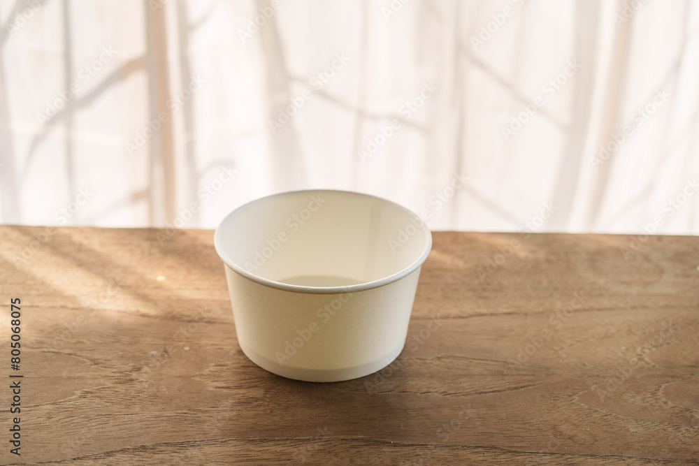 A food paper bowl rests on a brown wooden desk indoors A food paper bowl rests on a brown wooden desk indoors