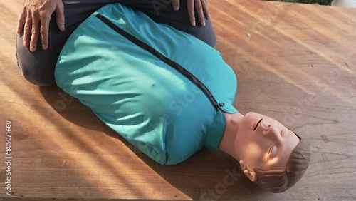 Close-up of middle-aged Asian male hands performing cardiopulmonary resuscitation (CPR) on a training dummy. Vital techniques include defibrillation, chest compressions, and maintaining the airway. photo