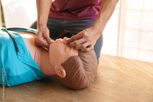 Close-up of middle-aged Asian male hands performing cardiopulmonary resuscitation (CPR) on a training dummy. Vital techniques include defibrillation, chest compressions, and maintaining the airway. photo