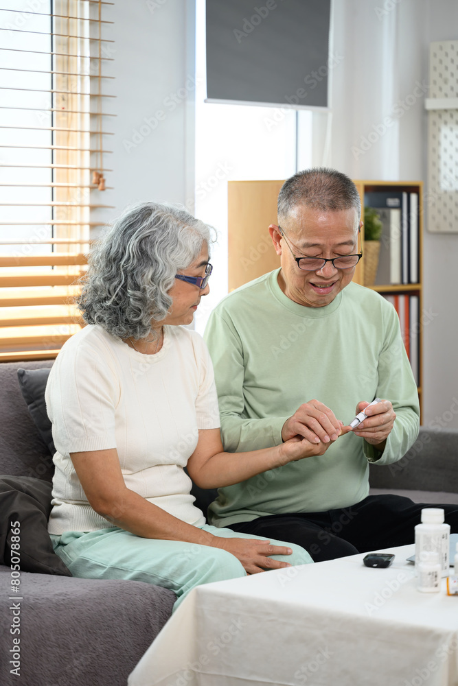 Obraz premium Caring mature man checking blood sugar of his diabetic wife at home. Elderly healthcare concept